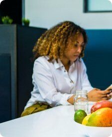 women looking at her phone and fruits in the background